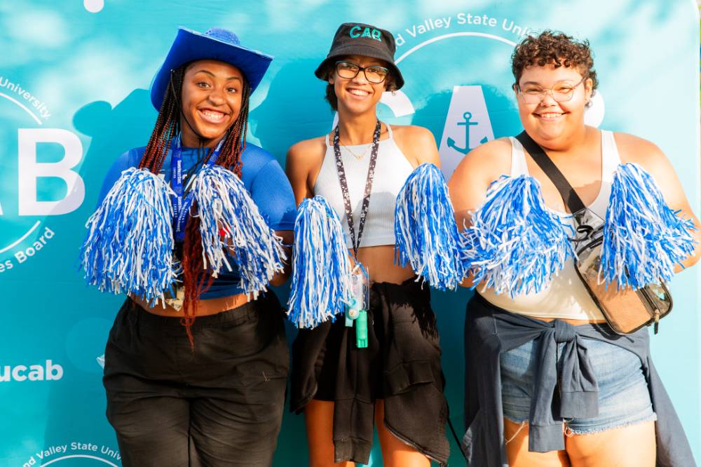 students posing in front of CAB backdrop at Laker Kickoff photo booth with pom poms